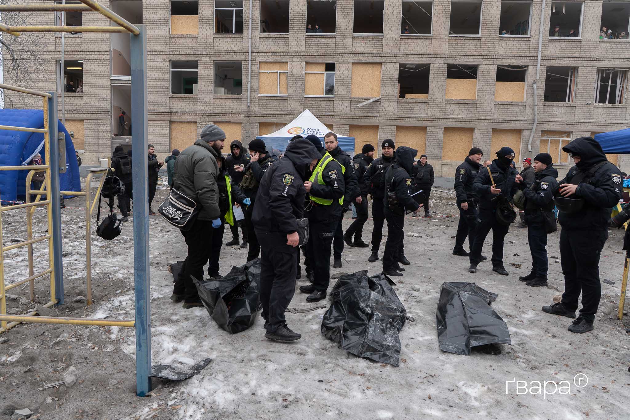 Поліціянти поряд з місцем удару російської ракети у Харкові, поряд з ними — три тіла загиблих людей, які жили в обстріляній п'ятиповерхівці.